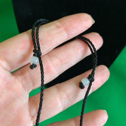Hand wearing a black cord necklace with a small round bead on a green background