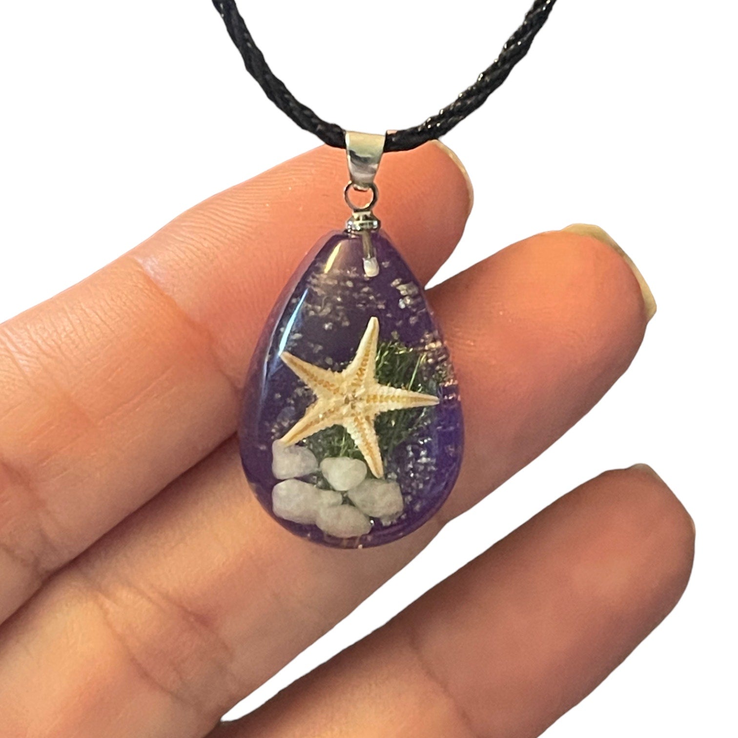 Purple charm with a starfish on a black cord being held by a hand on a white background