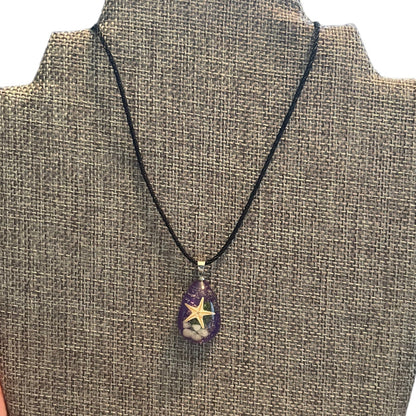 A black cord necklace with a teardrop-shaped purple pendant featuring a starfish design, displayed on a burlap-covered jewelry bust.