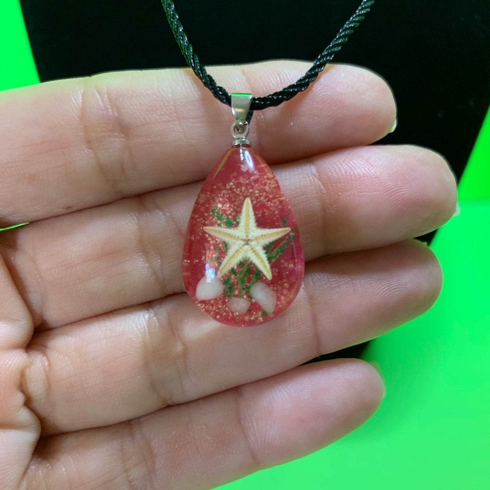 Teardrop-shaped pendant with star design held in a hand against a green background