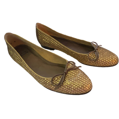 A pair of gold metallic flat shoes with a textured, sequined surface and brown leather bows on the toes, shown against a plain white background.