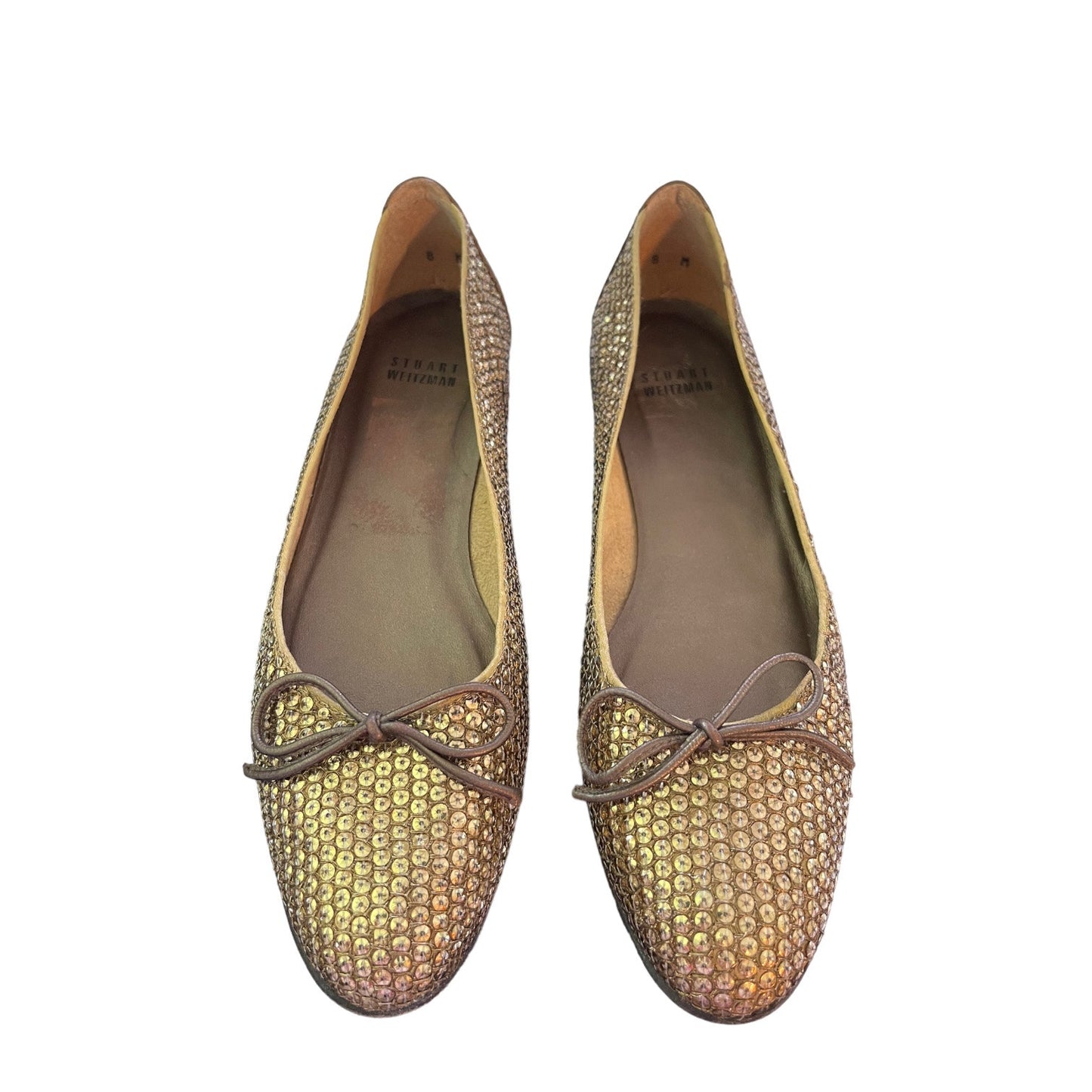 A pair of flats covered in gold-toned sequins with a leather bow on the front, shown against a plain white background.