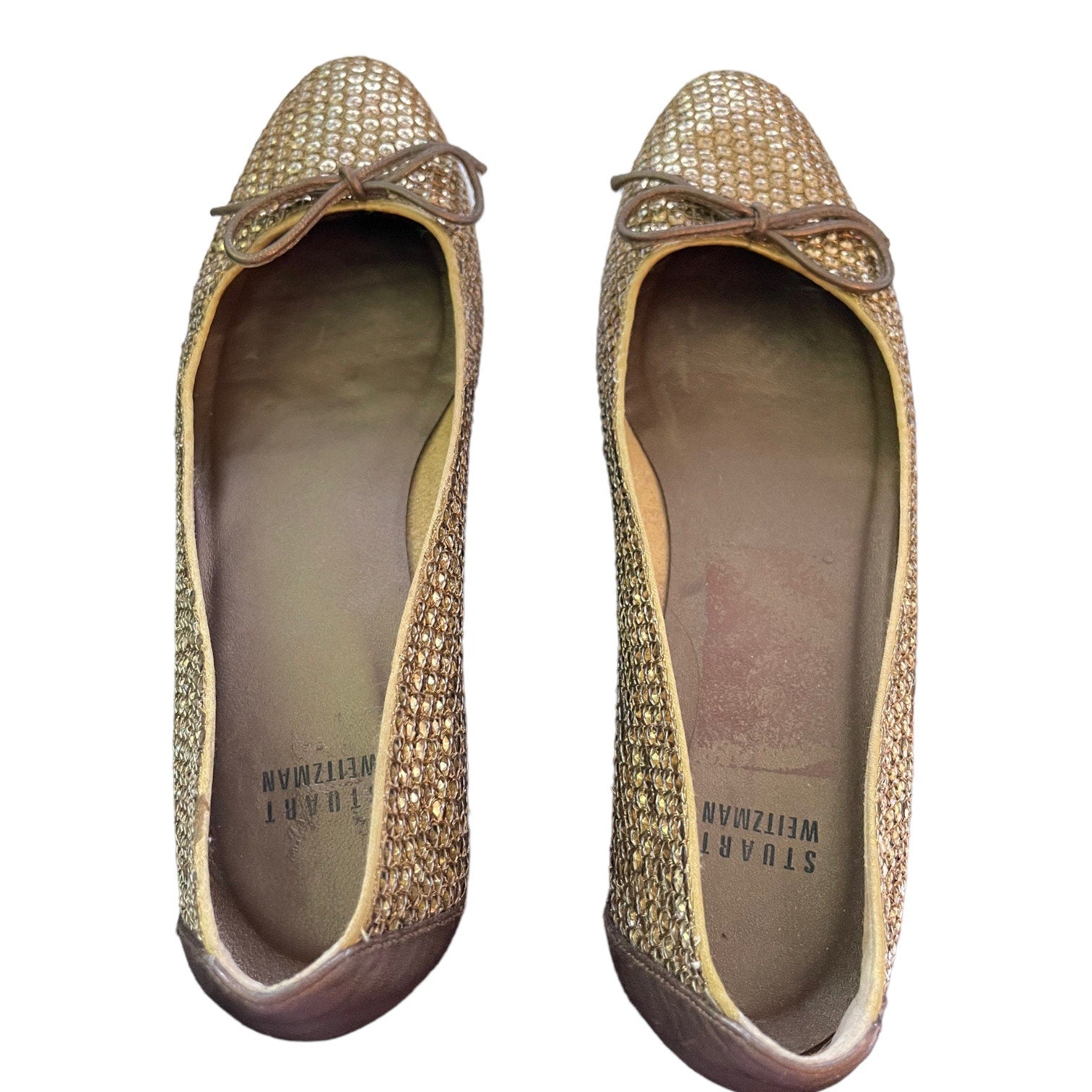 A pair of women's flats by Stuart Weitzman, featuring a textured gold sequined upper, a small brown bow at the toe, shown against a plain white background.