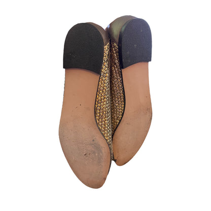 A pair of women's slip-on flats shown from the sole, featuring a tan leather base, a textured gold and black patterned insole, and a black heel cap.