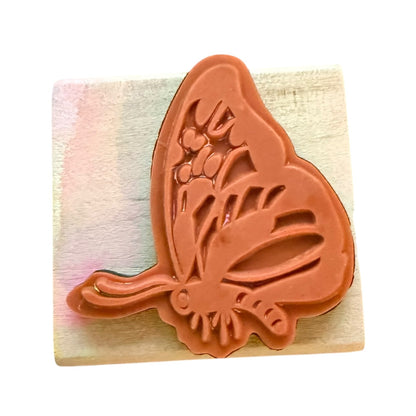 Butterfly-shaped stamp on a wooden block with a colorful striped background