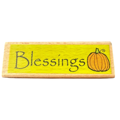 Wooden stamp with 'Blessings' and a pumpkin illustration on a yellow background