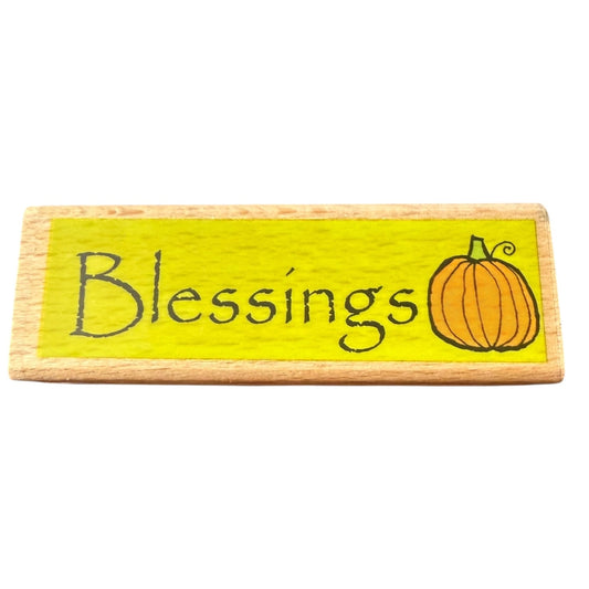 Wooden stamp with 'Blessings' and a pumpkin illustration on a yellow background