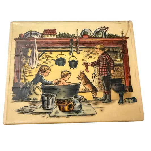 A wood rubber stamp featuring a detailed illustration of a family scene in a warm, cozy fireplace. The scene shows a girl washing a baby in a bathtub, a boy standing by the fire , and a dog, all rendered in a classic hand-painted style.