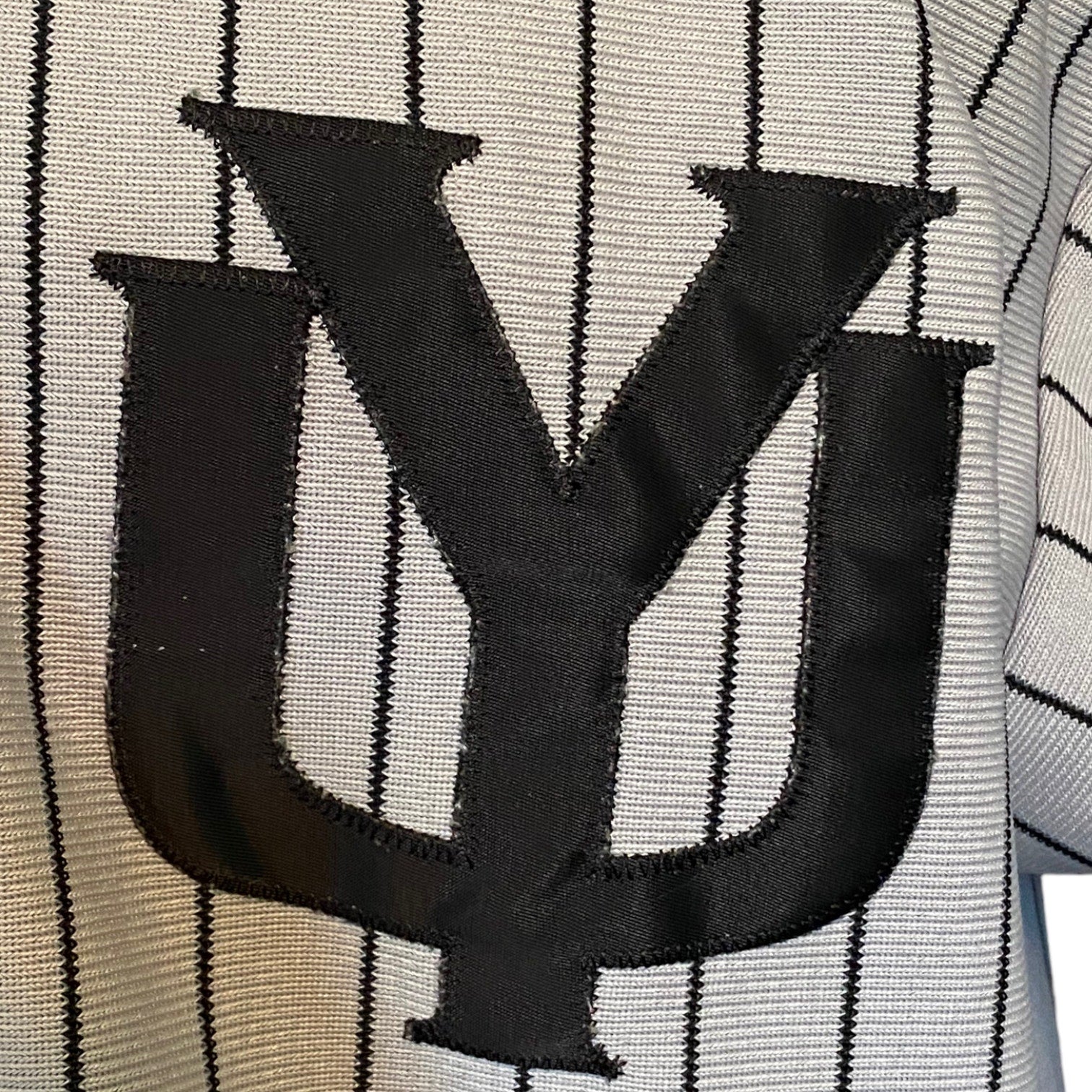 Close-up of a black embroidered stylized 'YU' logo on a gray pinstriped knit fabric.