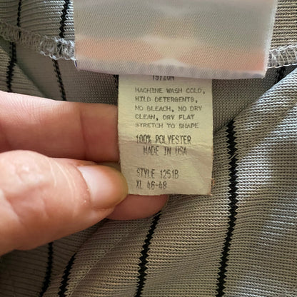 A close-up of a hand holding a garment's inner care label, showing details like '100% Polyester', 'Made in USA', and care instructions against a striped gray and black fabric background.
