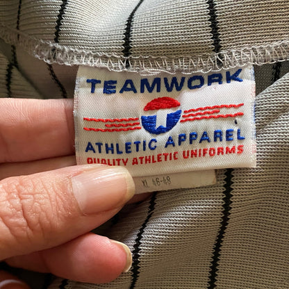 A close-up of a vintage Teamwork Athletic Apparel uniform label held by a hand, showing the brand logo and size 
