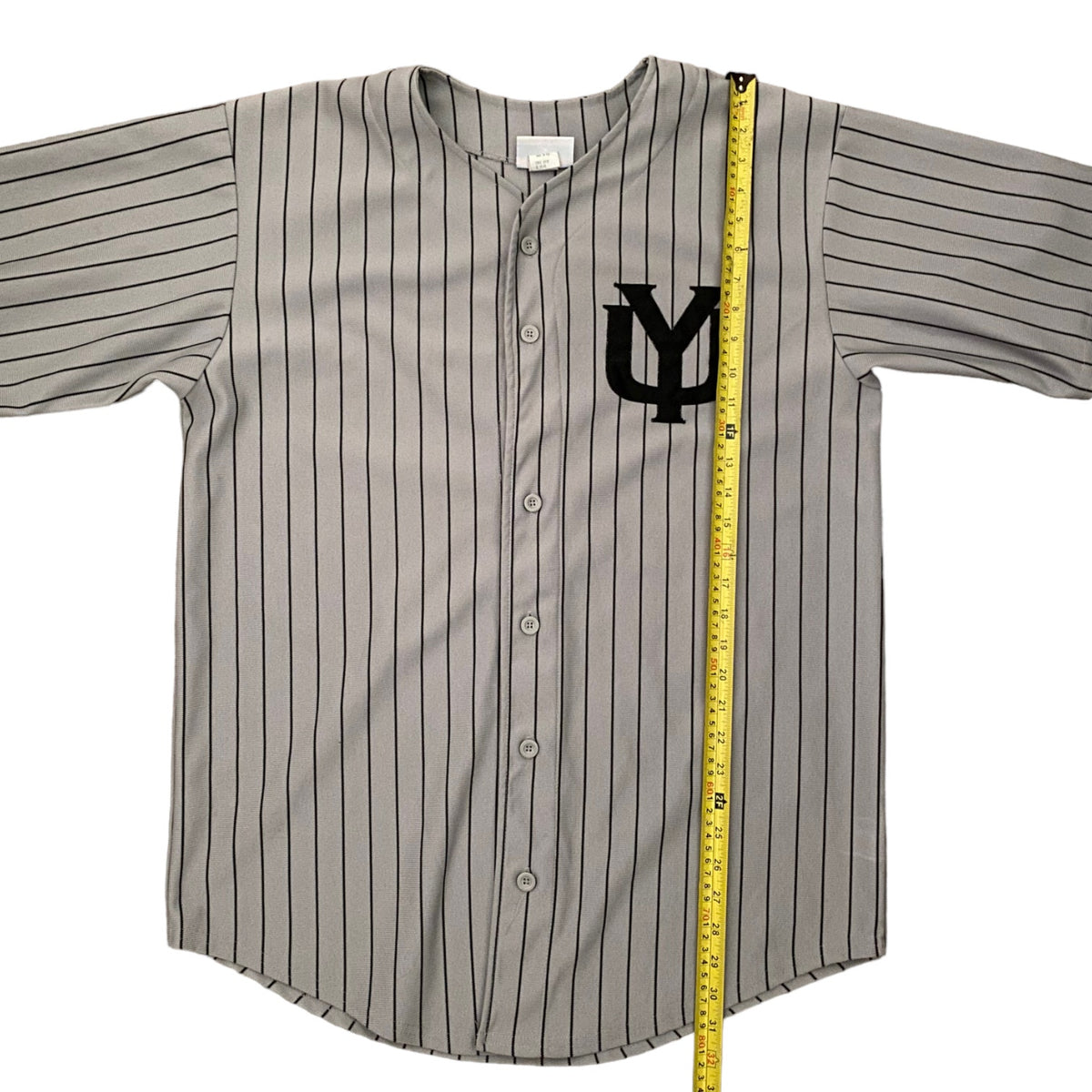 A gray short-sleeve pinstripe baseball jersey with a black 'YM' logo on the chest, laid flat with a yellow measuring tape running vertically along the right side.