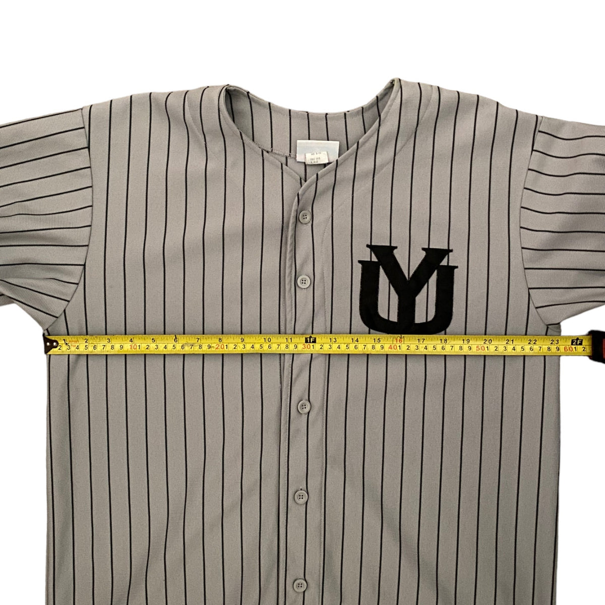 A gray pinstripe baseball jersey with a black 'YU' logo on the chest, shown with a yellow tape measure stretched horizontally across the chest to indicate width.