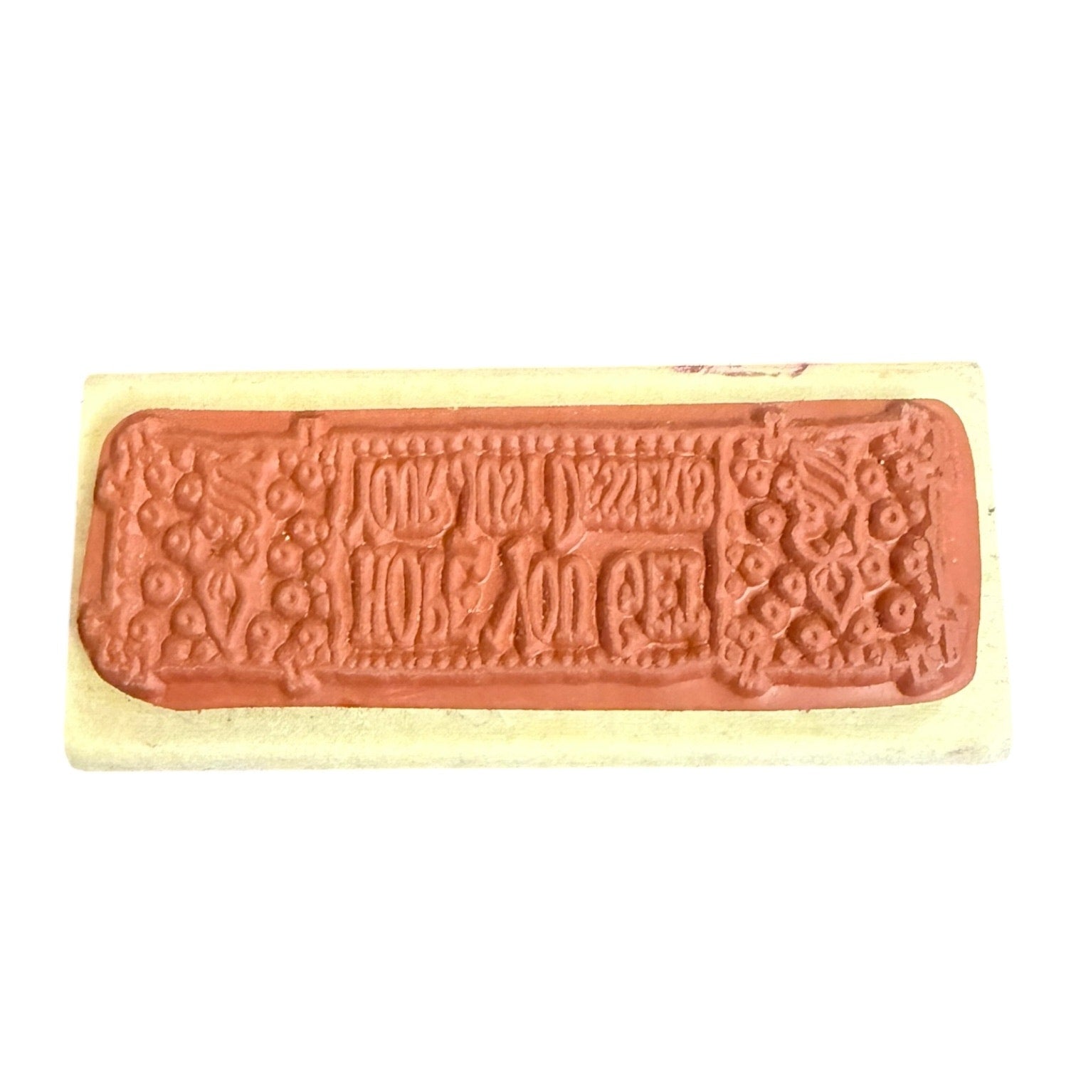 A rectangular stamp with an embossed  design, set against a light beige background on a plain white studio backdrop.