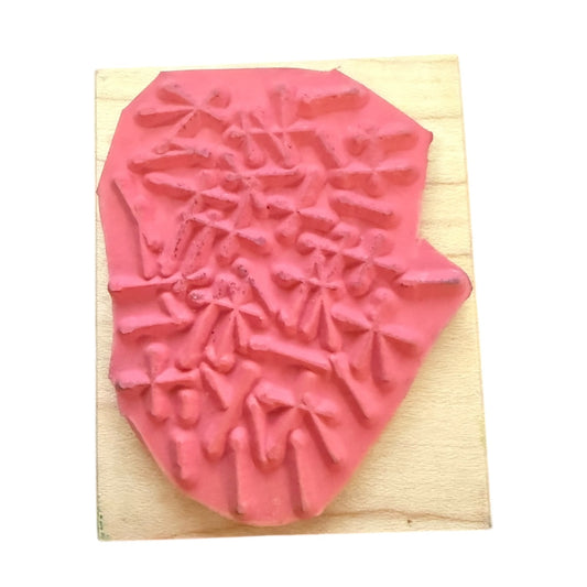 A pink rubber stamp with an abstract line pattern, mounted on a light-colored wooden block against a white background.