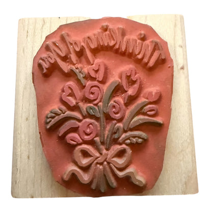 A terracotta-colored rubber stamp with a floral bouquet and bow design, mounted on a square light wood block against a white background.