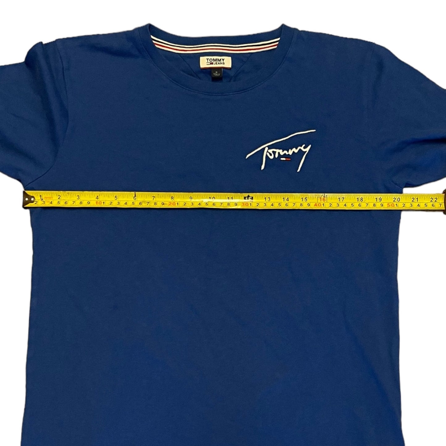 Blue Tommy Hilfiger t-shirt with a measuring tape across it on a white background