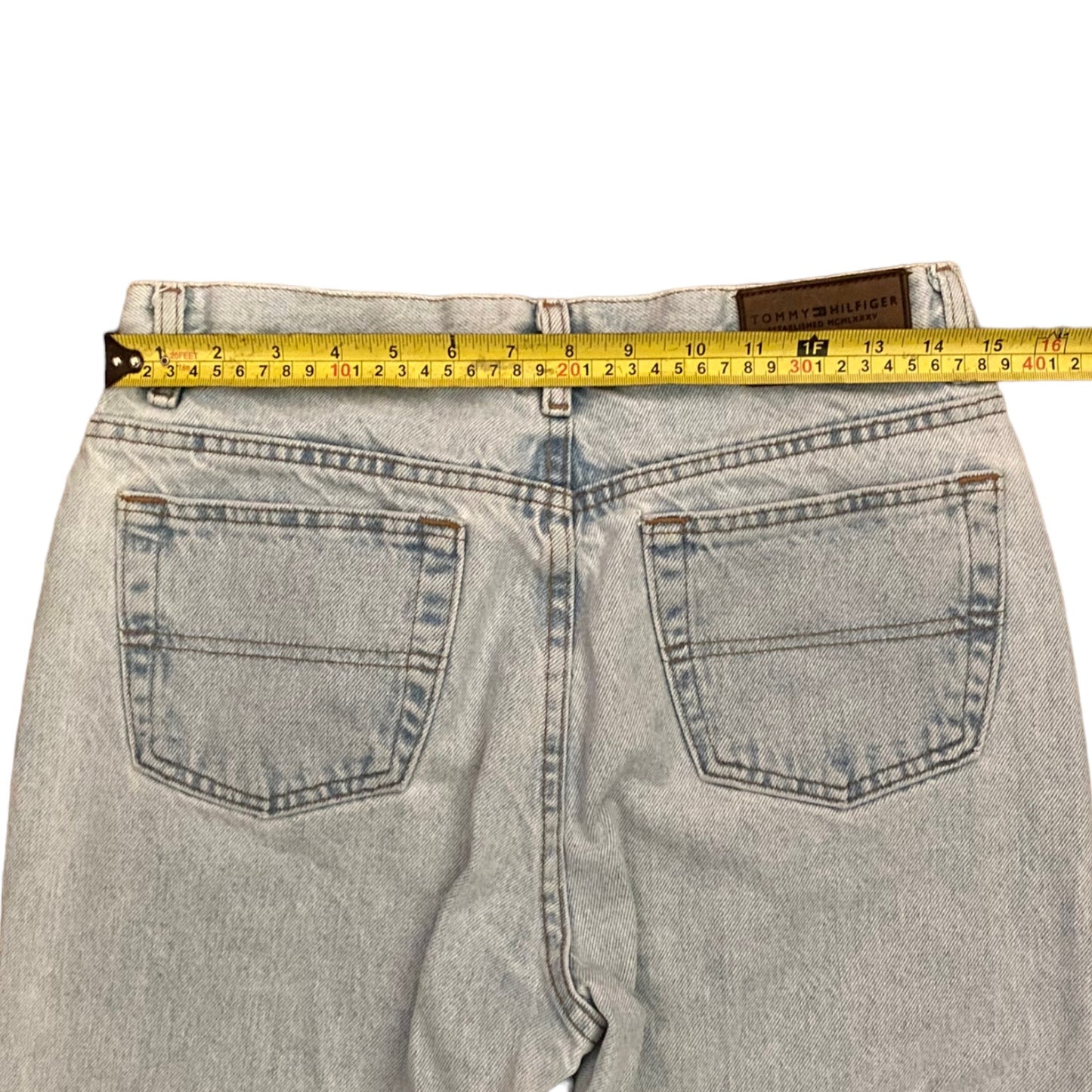 Back view of light-wash denim jeans with a yellow tape measure stretched across the waistband to show the measurement.