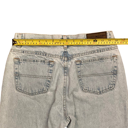 Back view of light-wash denim jeans with a yellow tape measure stretched across the waistband to show the measurement.