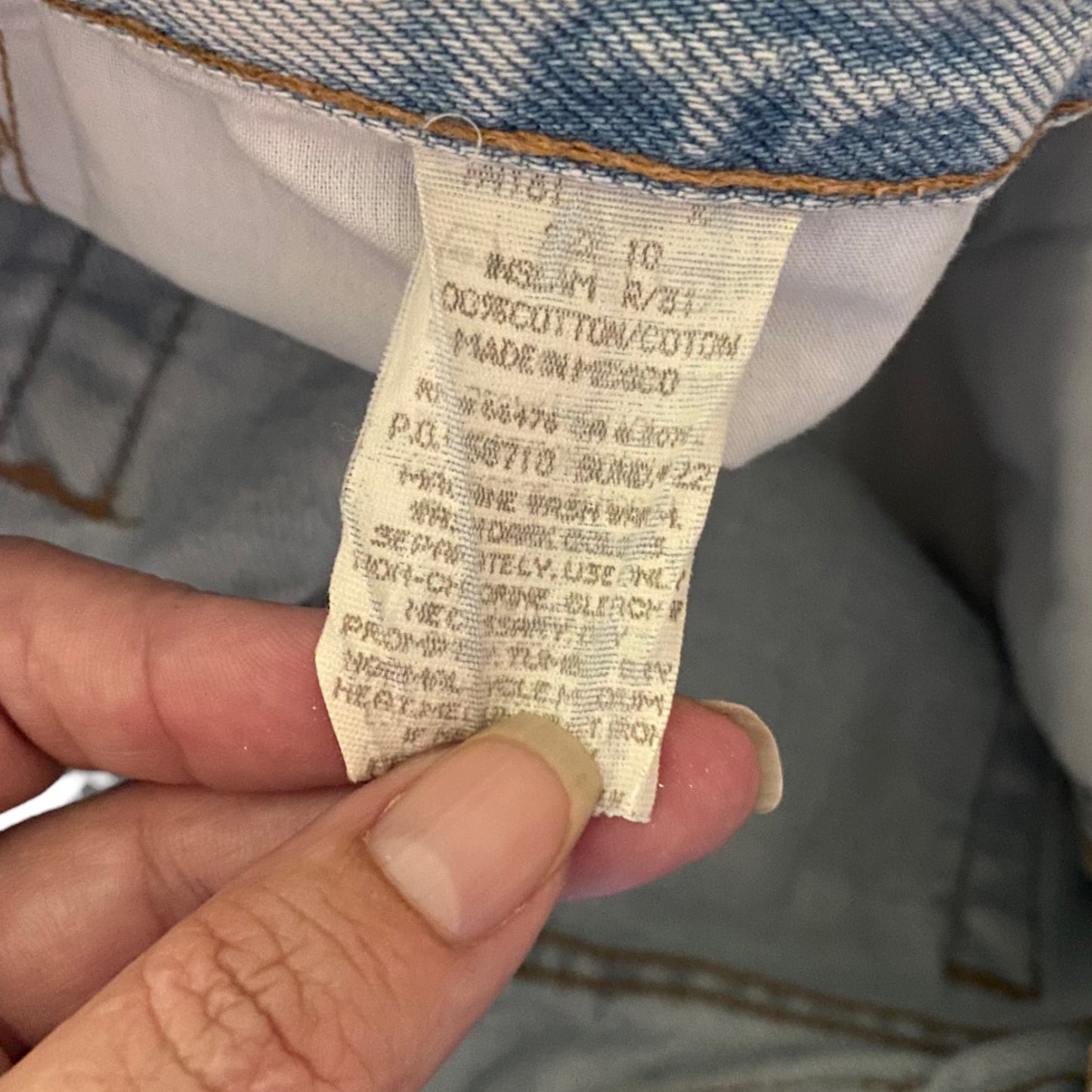 A close-up of a hand holding a sewn-in cotton size and care label on a pair of blue denim jeans.