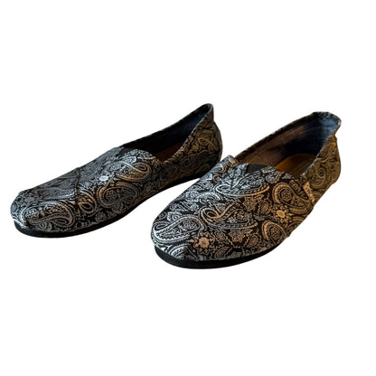 A pair of slip-on loafers with an intricate black and silver paisley pattern, displayed against a plain white background.