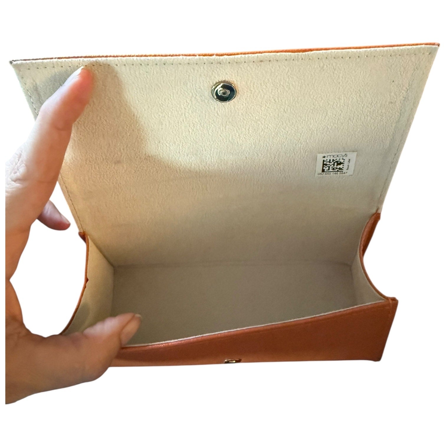 A hand holding open a orange and cream eyeglass case, showing the interior lining, snap button closure, and a small product label.