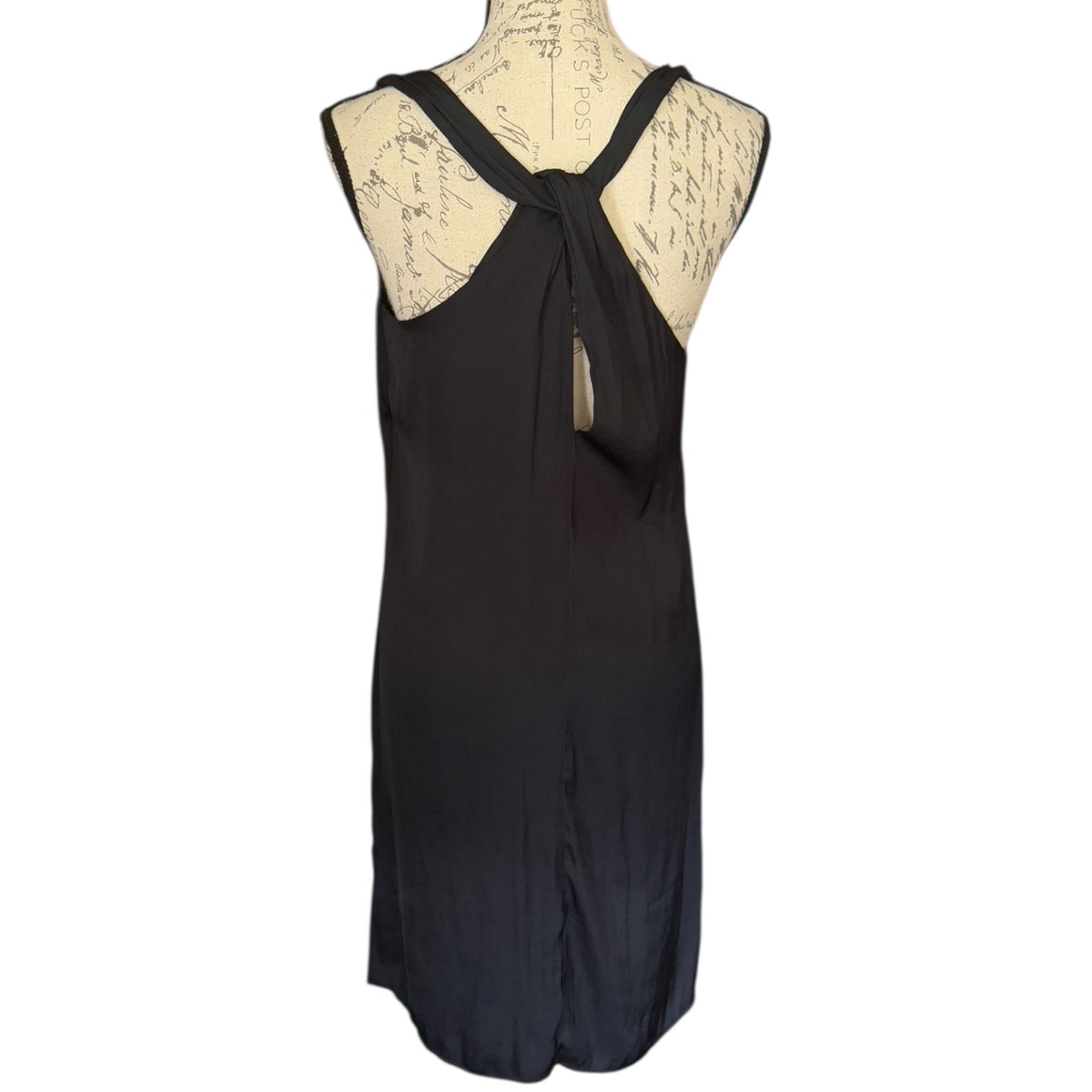 A sleeveless black dress from the back displayed on a cream-colored dress form mannequin against a plain white background.