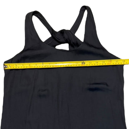 A black racerback tank dress with a crossover back design, shown with a yellow measuring tape stretched horizontally across the chest to indicate the garment's width.