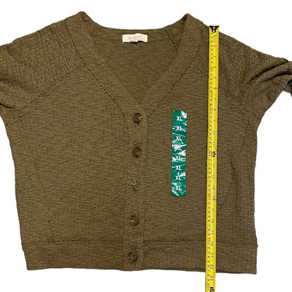 An green knit cardigan sweater laid flat on a white background, shown with a yellow tape measure along the right side for size reference. The cardigan has a V-neck, short sleeves, and front buttons.