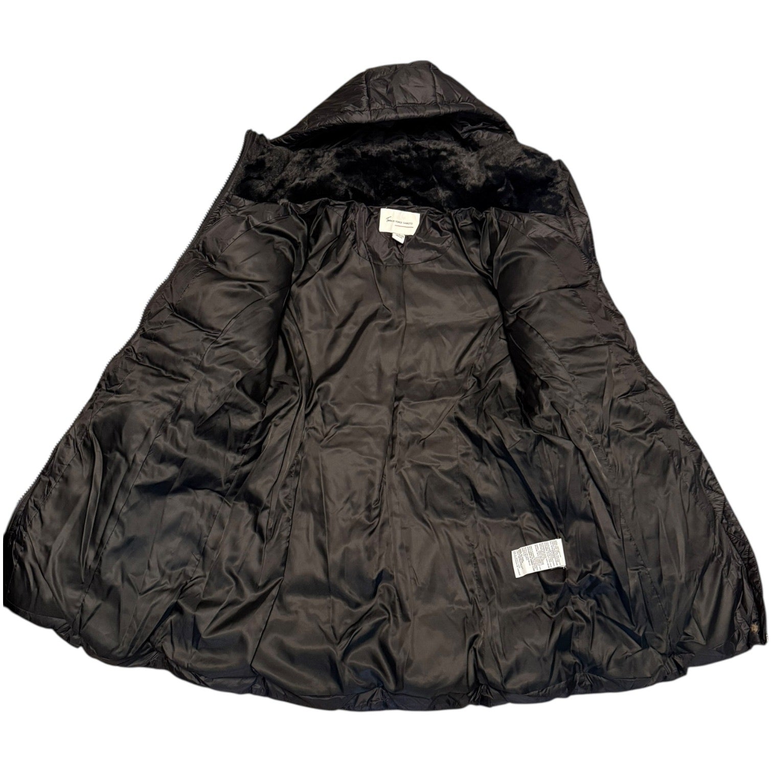 A black quilted puffer jacket with a plush black faux-fur hood lining, laid flat against a white background. Two small white brand labels are visible on the interior.