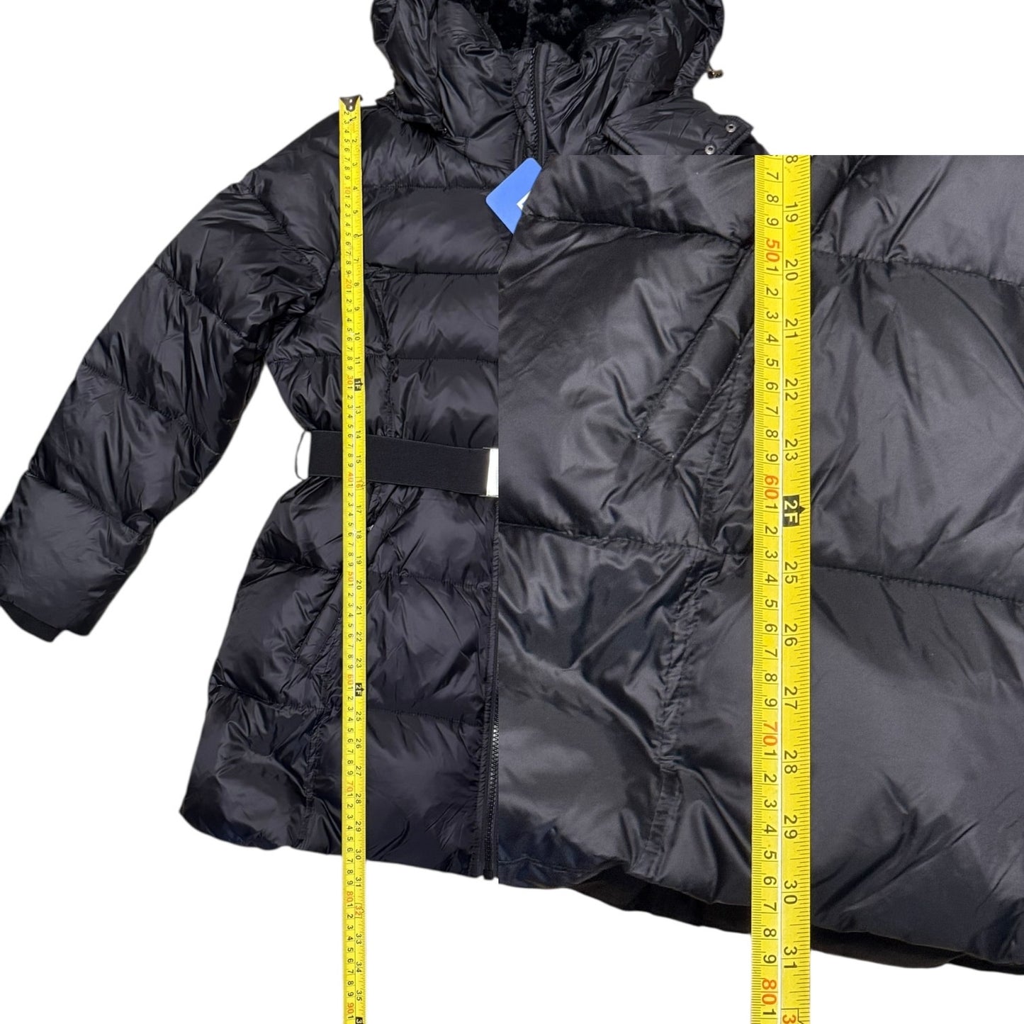 A black quilted puffer jacket shown on a white background with yellow measuring tape standing vertically to indicate dimensions.
