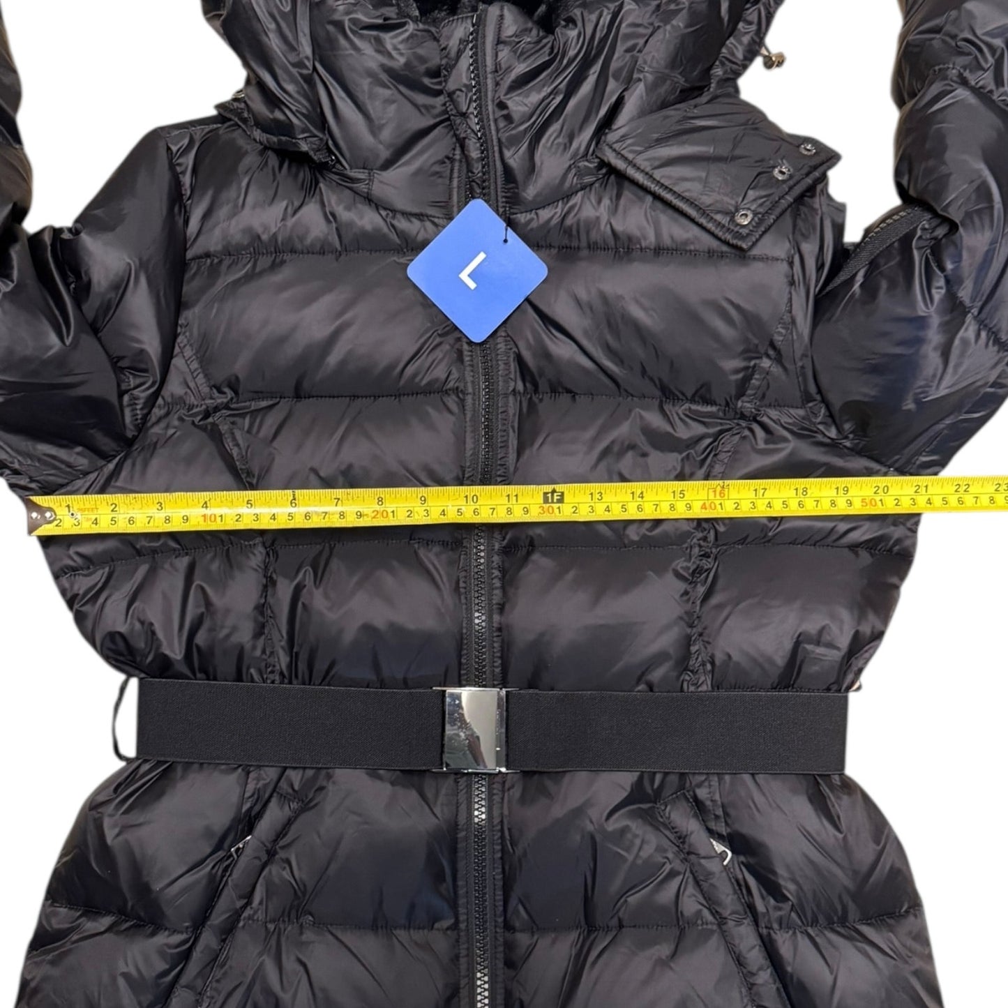 A black puffer jacket with a waist belt and front zipper, shown with a yellow measuring tape across the chest and a blue size tag labeled 'L'.