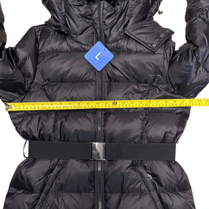A black puffer jacket with a waist belt and front zipper, shown with a yellow measuring tape across the chest and a blue size tag labeled 'L'.