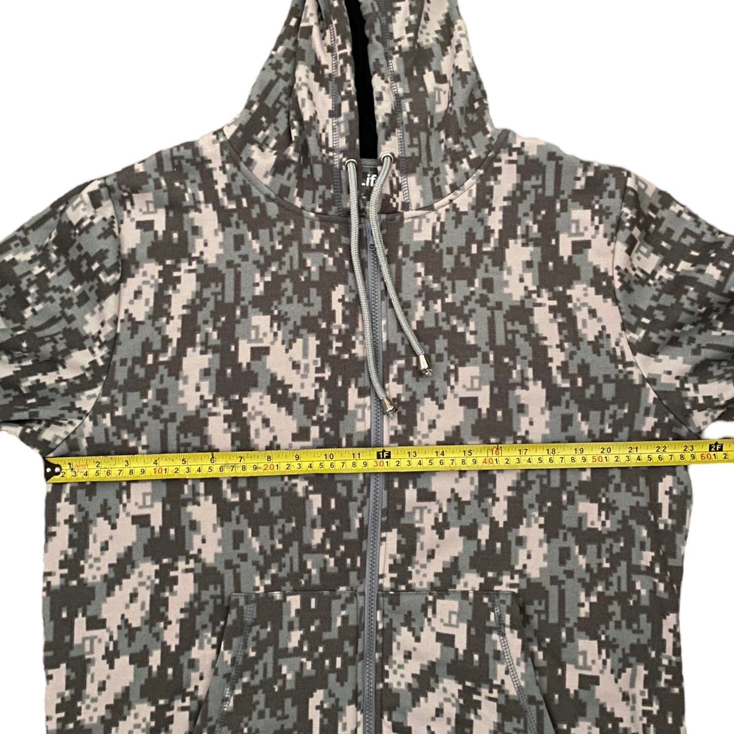 A hooded zip-up jacket with a digital camouflage pattern, shown with a yellow tape measure stretched horizontally across the chest to indicate size.