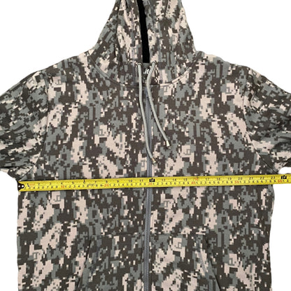 A hooded zip-up jacket with a digital camouflage pattern, shown with a yellow tape measure stretched horizontally across the chest to indicate size.