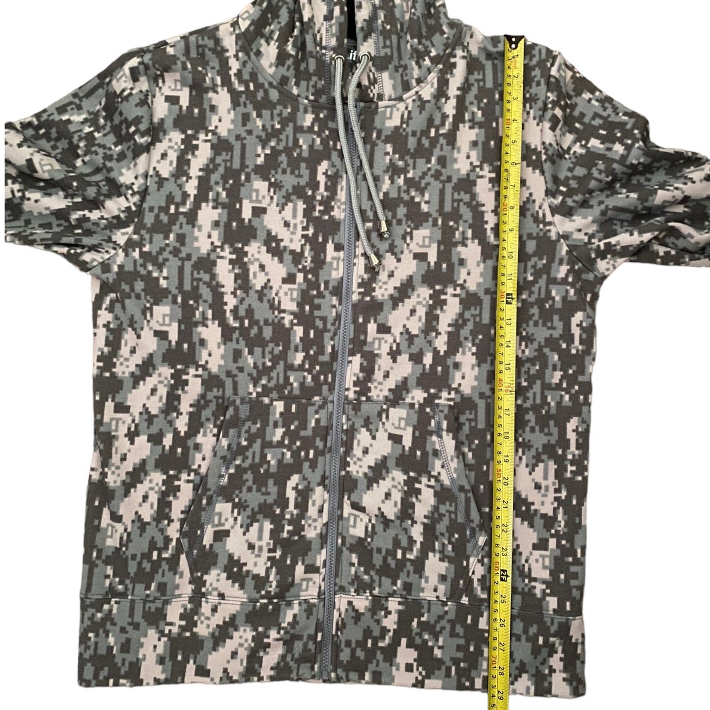 A zip-up hoodie with a digital camouflage pattern, shown flat with a yellow tape measure standing vertically on the right side for scale.
