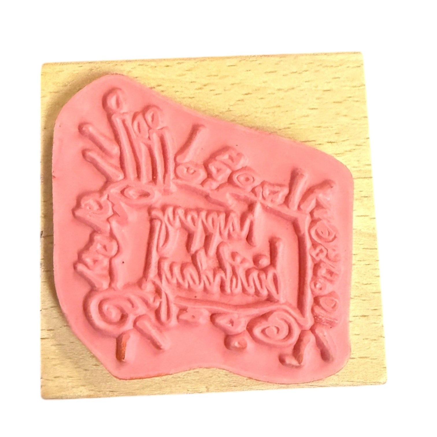 A pink rubber stamp, mounted on a square light wood block against a white background.