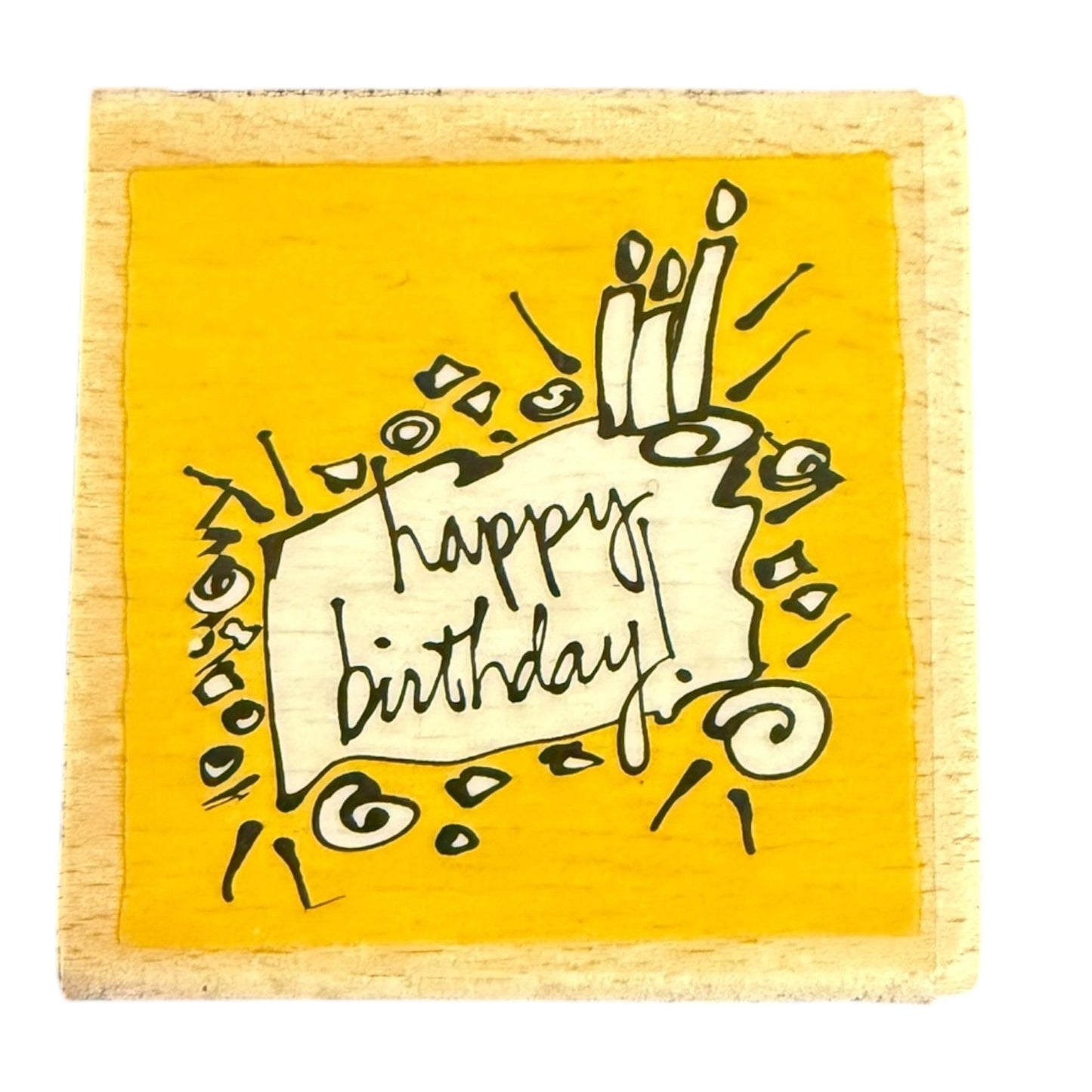 A square wooden block stamp featuring a bright yellow face with a hand-drawn black ink illustration of candles, confetti, and a banner reading 'Happy Birthday!'.