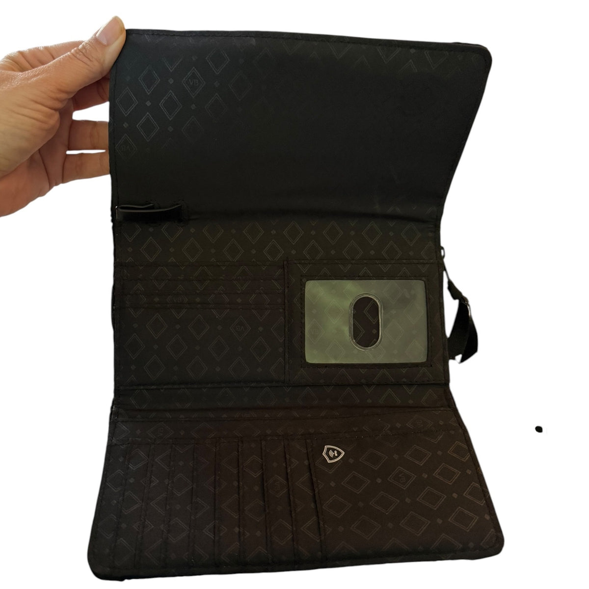 Black interior of purse of a black purse with a hand holding it open on a white background. 