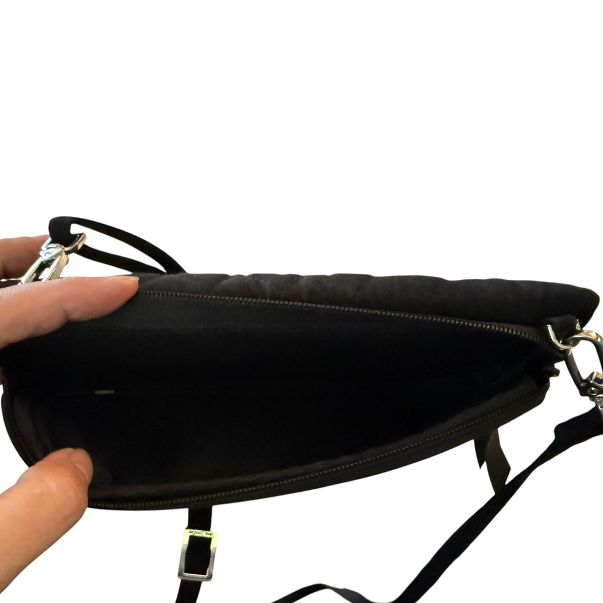 Hand holding open a black purse with a zippered pocket, showing that pocket open on a white background. 