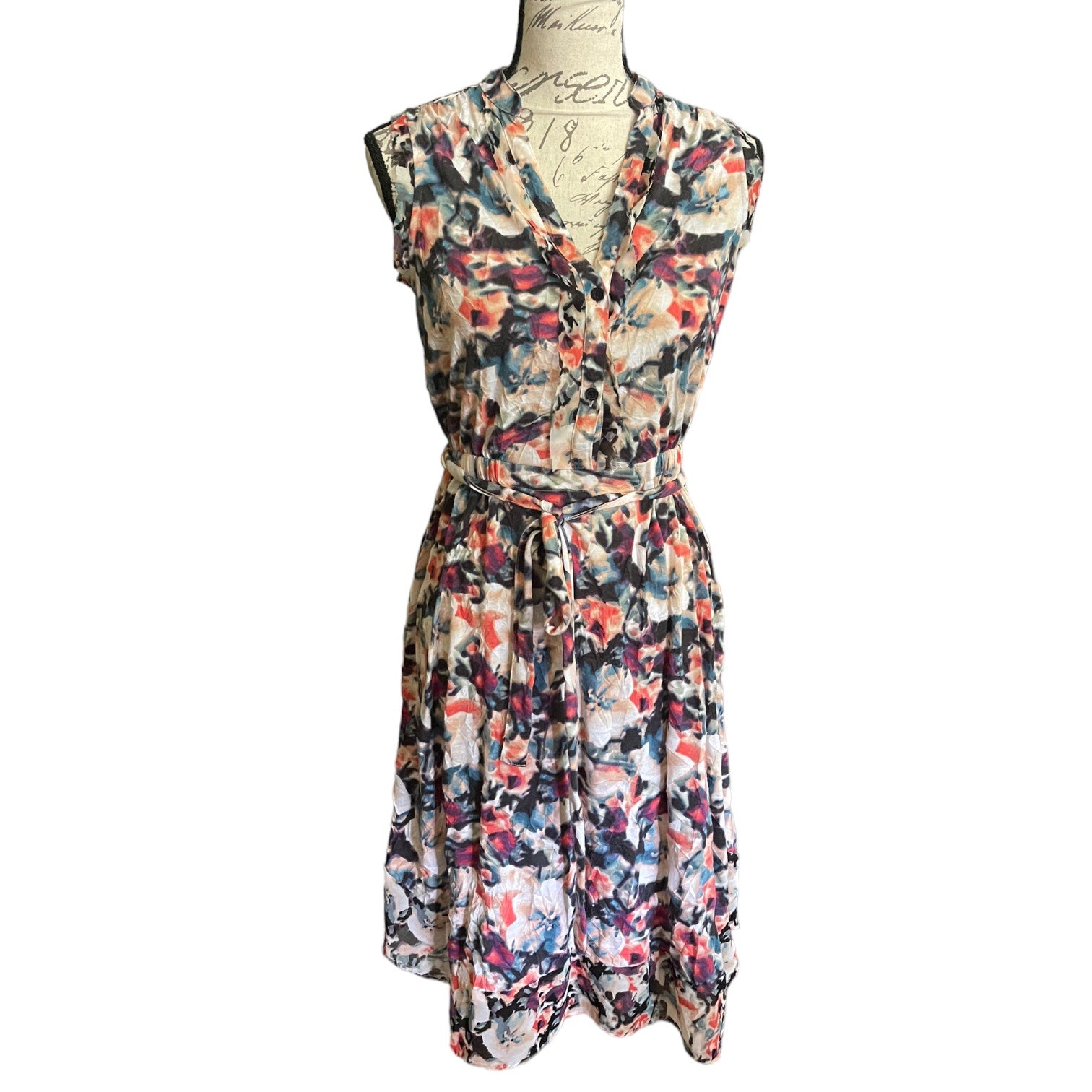 A sleeveless V-neck dress with a tie-front waist and a colorful abstract floral print, displayed on a dress form against a white background.