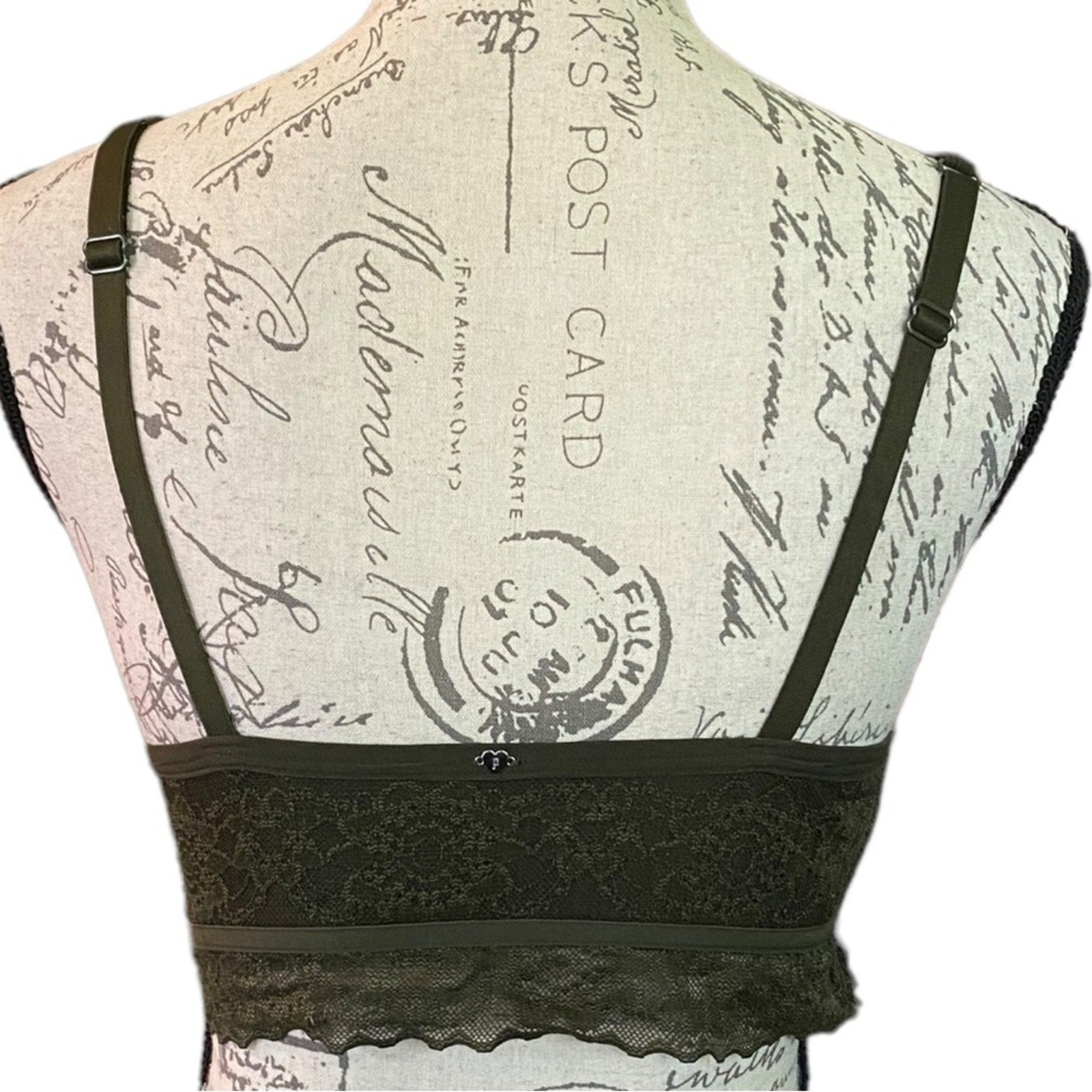 An green lace bralette displayed on a vintage-style printed dress form mannequin, showing the back view with shoulder straps and a lace underband.