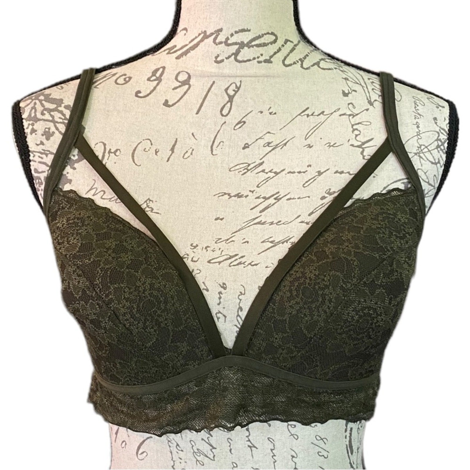green lace bra with thin adjustable shoulder straps and a wide underband, displayed on a vintage-style mannequin torso with cursive script background.