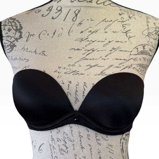 Black strapless bra displayed on a beige dress form with a cursive script print, against a white background.