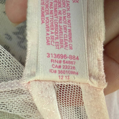 Close-up of a garment's interior neck label with pink printed text and numbers on a white mesh fabric, held by fingers.