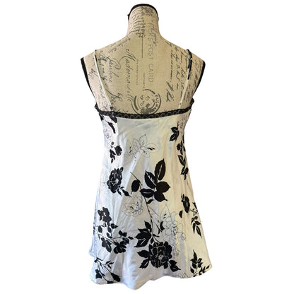A sleeveless white babydoll nightgown with a black floral print, displayed on a vintage-style paper-covered dress form mannequin against a white background.