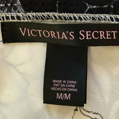 Close-up of a Victoria's Secret garment label attached to a black lace trim and white fabric, with the brand name in pink on the black tag.