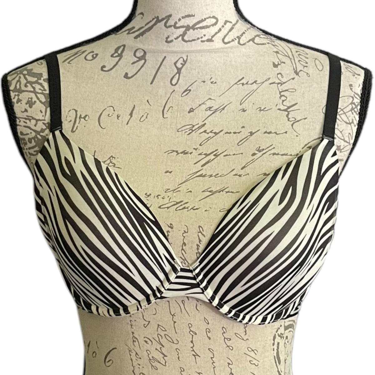 Black and white zebra-print bra displayed on a beige fabric dress form with a cursive script print, against a plain white background.