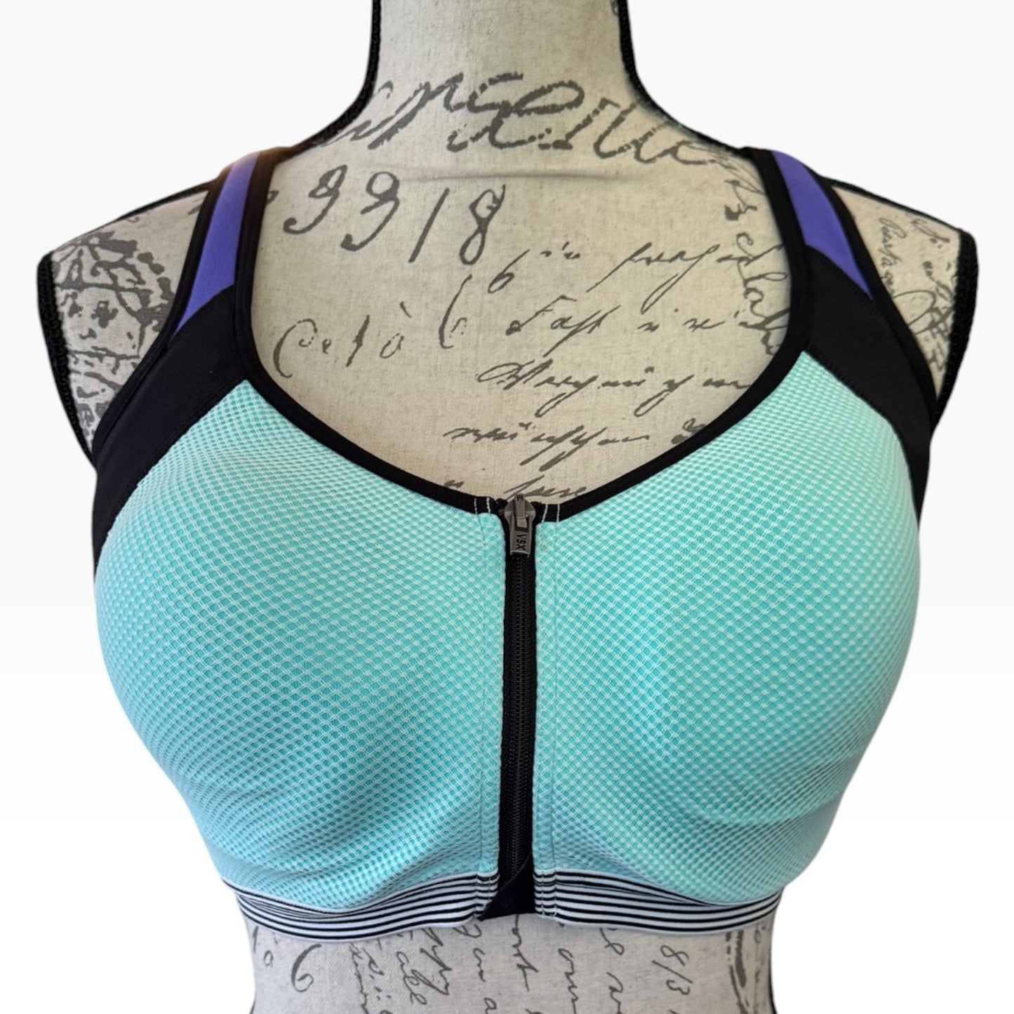 A women's mesh zip-front sports bra in blue, puple and black, displayed on a vintage-style mannequin torso with cursive writing.