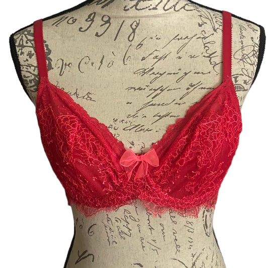 Red lace bra with a small bow at the center front, displayed on a vintage-style mannequin torso with cursive script print.